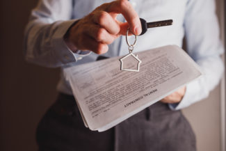 Manager offers keys to house holding rental contract in other hand. Rent and buying a property