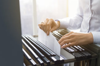 Professional female office clerk searching files and paperwork in the filing cabinet